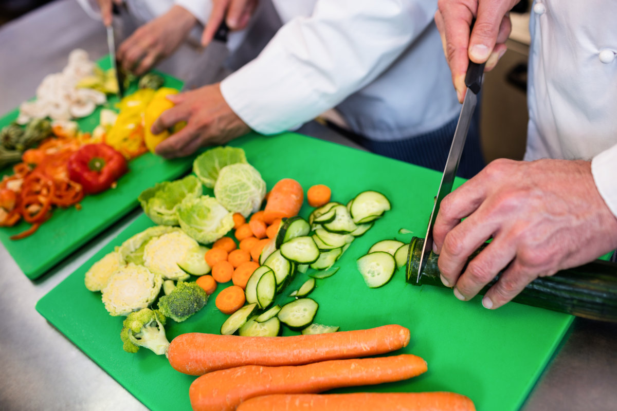 Close-up of chefs chopping vegetables on chopping board in the kitchen